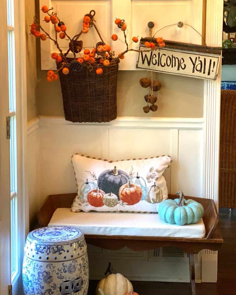 Charming rustic entryway with a wooden bench, festive pumpkin decor, a woven basket with autumn branches, and a welcoming farmhouse sign