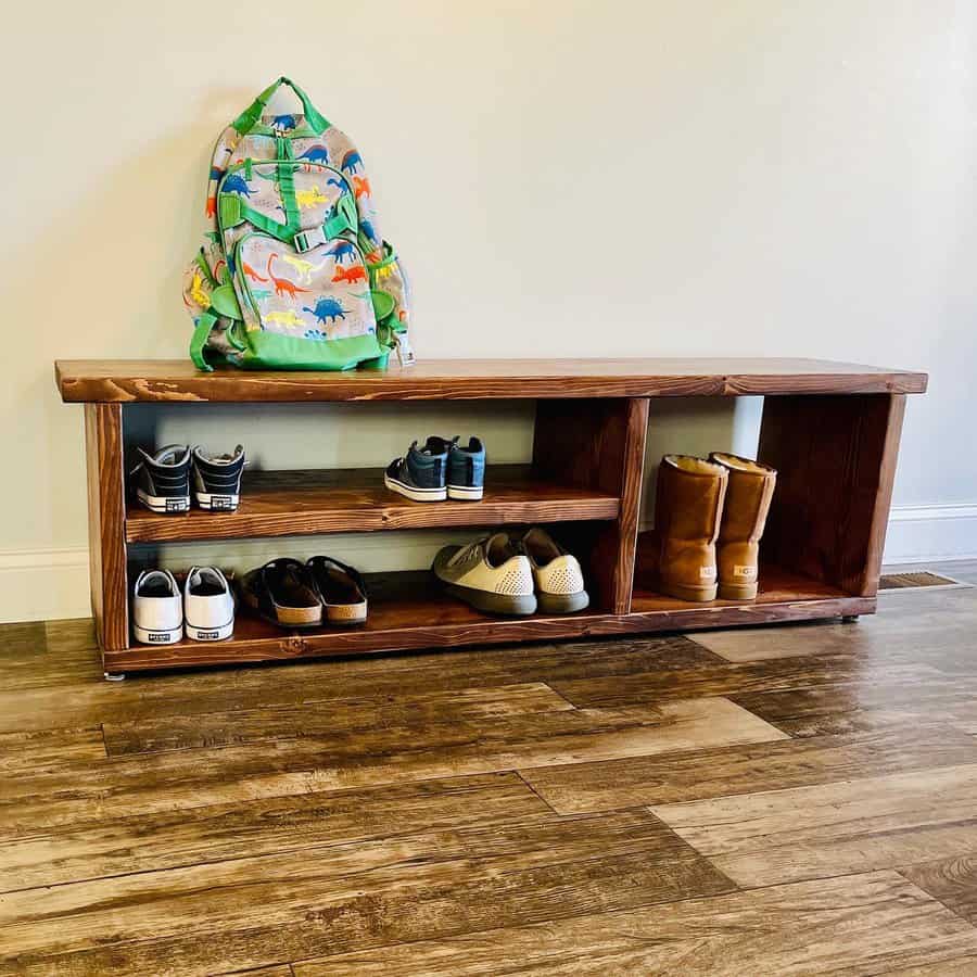 Wooden shoe rack with various shoes and a colorful dinosaur backpack on it, placed on a wooden floor