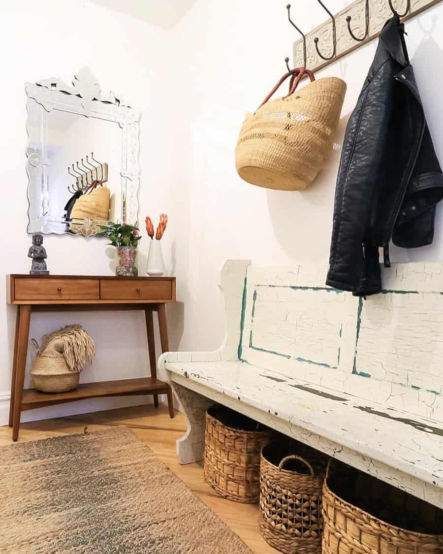 Hallway with a wooden bench, hanging black jacket, woven baskets, a mirror, a vase with flowers, and a wooden console table