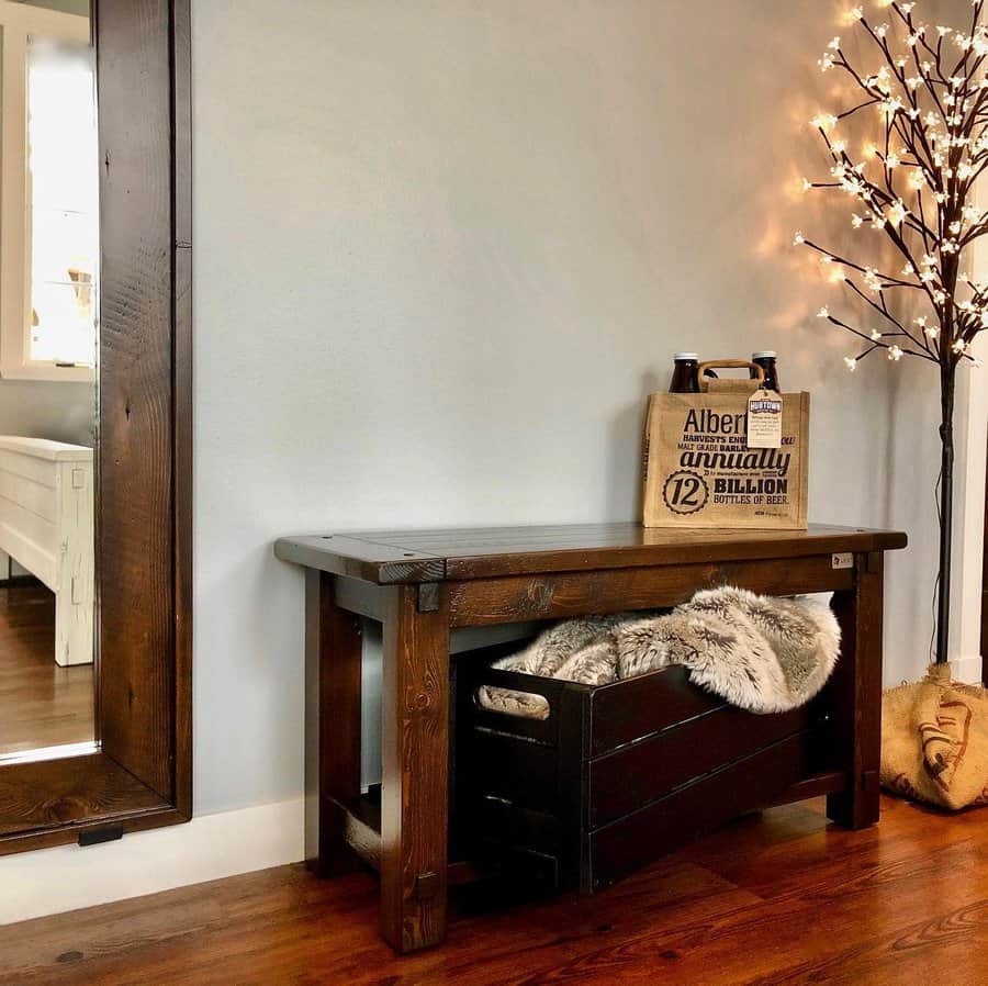 Cozy entryway with a wooden bench, faux fur blanket in a crate underneath, a lit branch decor, and a decorative paper bag