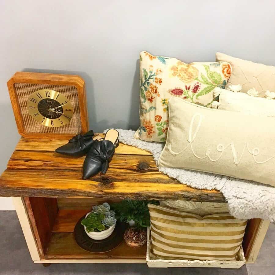 Wooden bench with cushions, black shoes, and a vintage clock on top; below is a potted plant and striped pillow