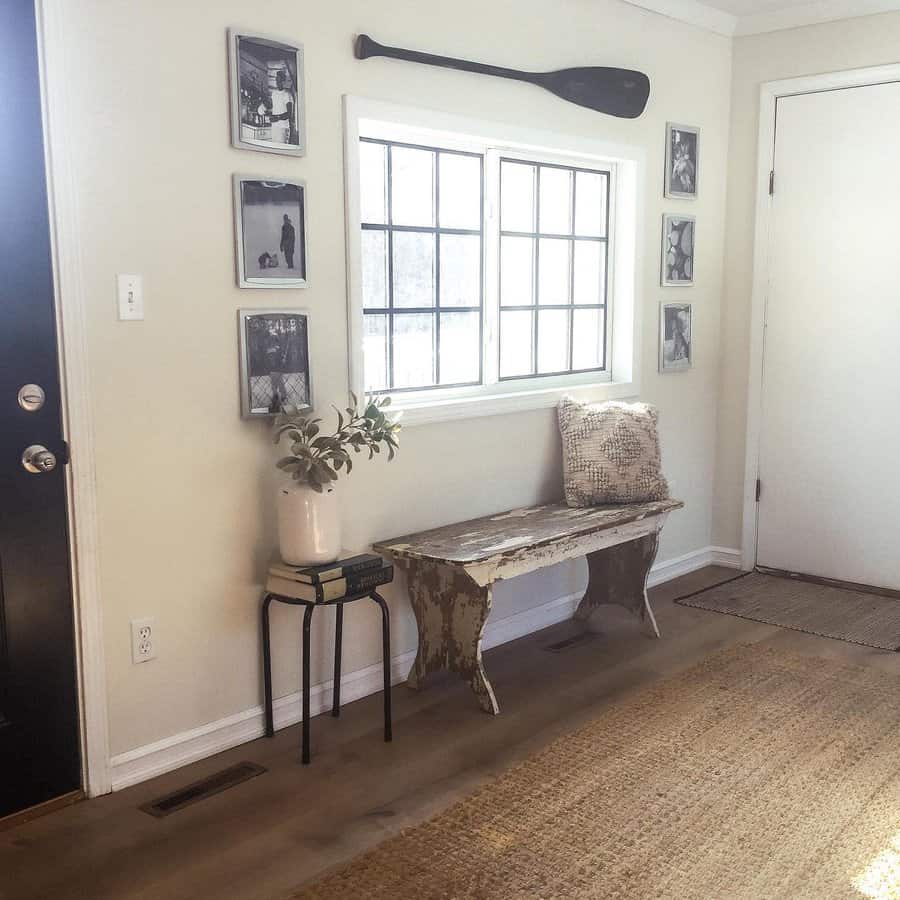 Rustic entryway with a wooden bench, framed photos, a decorative paddle, a potted plant, and a beige rug near a window and white door