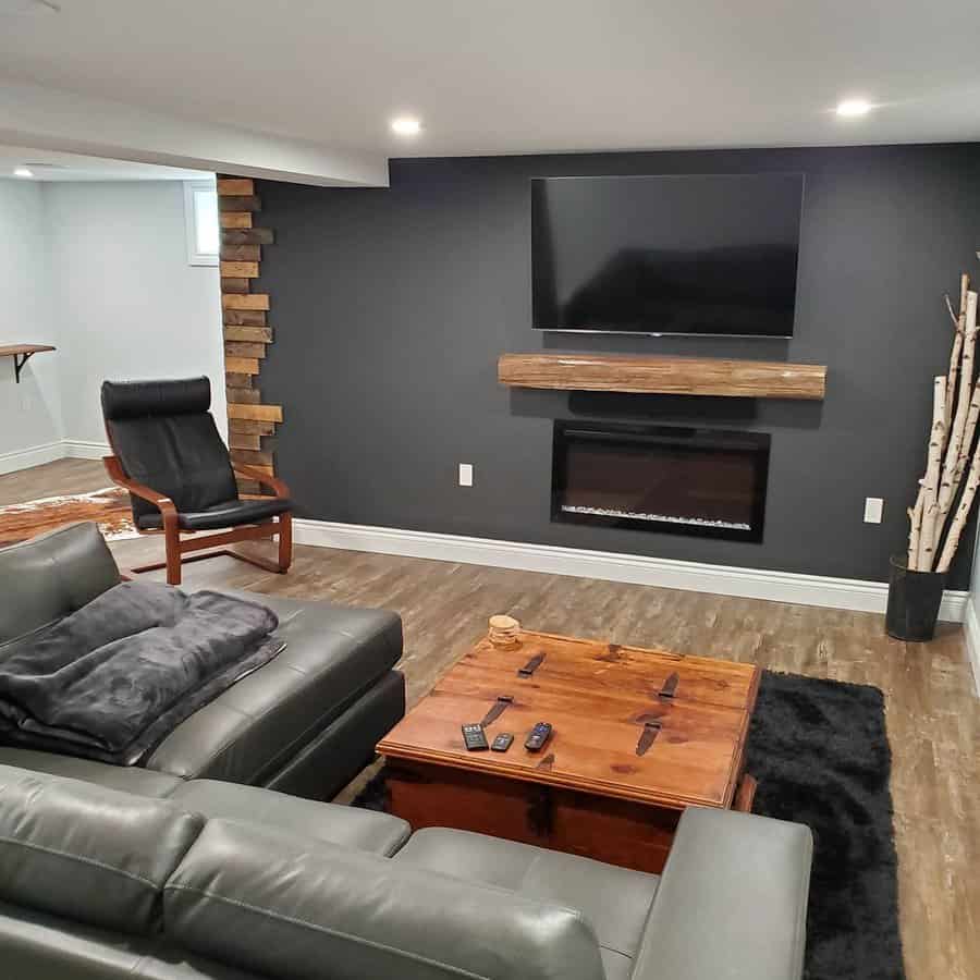 Cozy rustic basement with a dark accent wall, built-in fireplace, leather seating, and wooden decor elements for a warm and inviting entertainment space.