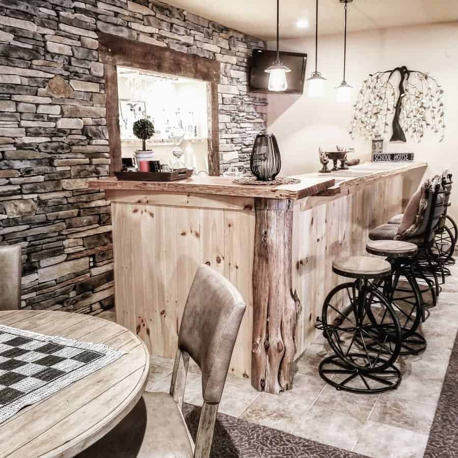 Rustic basement bar with a live-edge wood counter, stone accent wall, unique bicycle-style barstools, and warm lighting for a cozy lodge-inspired feel.