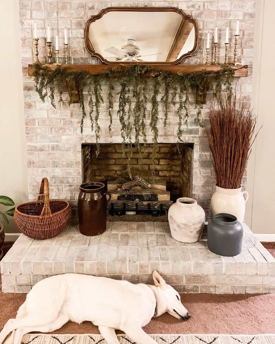 Cozy fireplace with hanging greenery and candles above; vases and baskets decorate the hearth, and a white dog sleeps on the floor