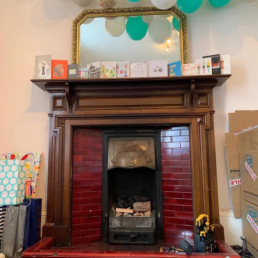 A rustic wooden fireplace with a gold-framed mirror, red tiles, and a cozy ambiance, decorated with birthday cards, gifts, and balloons for a festive touch