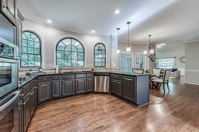 Warm hardwood flooring enhances this elegant kitchen, complementing dark cabinetry and arched windows for a timeless and inviting rustic charm