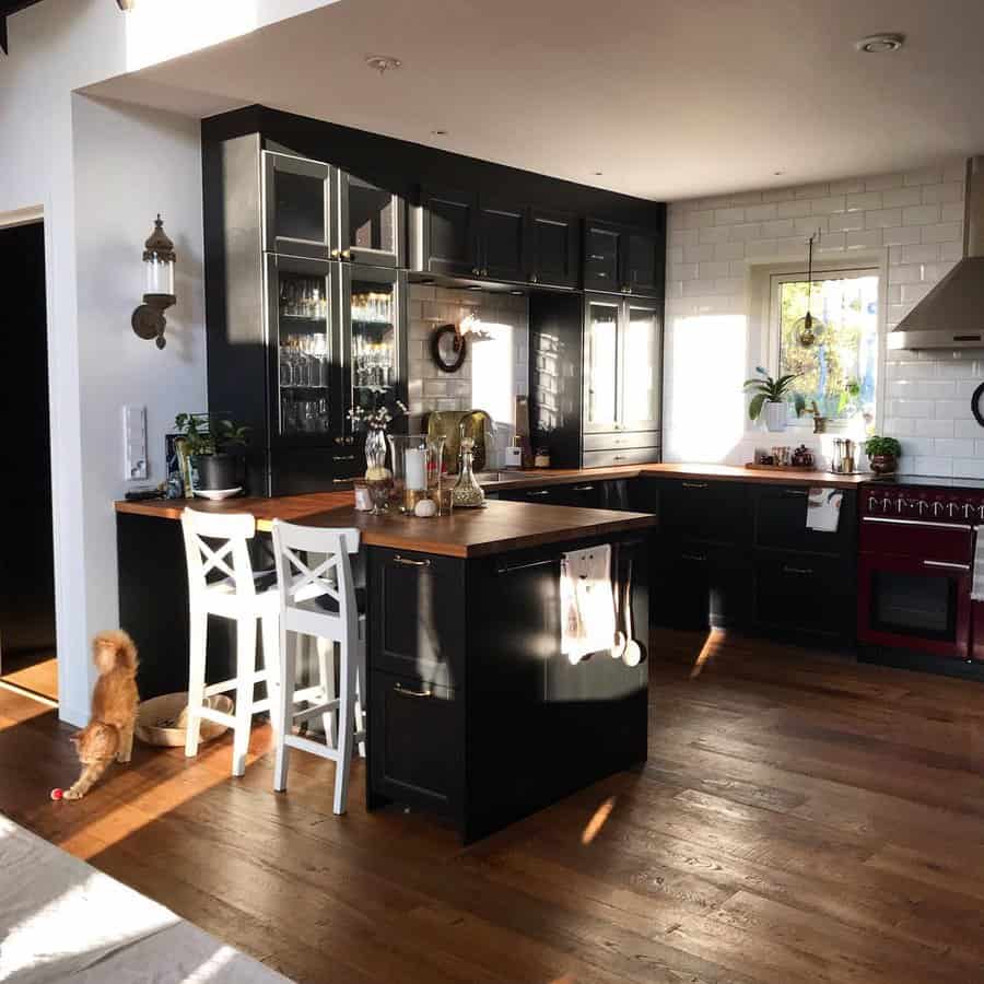 Rich hardwood flooring enhances this cozy rustic kitchen, complementing black cabinetry, wood countertops, and warm natural light for a timeless feel