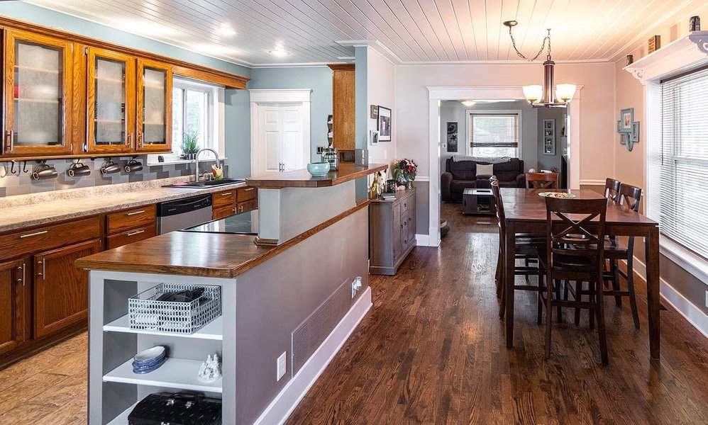 Open kitchen and dining area with wooden cabinets, hardwood floors, and a dining table; bright natural light from large windows