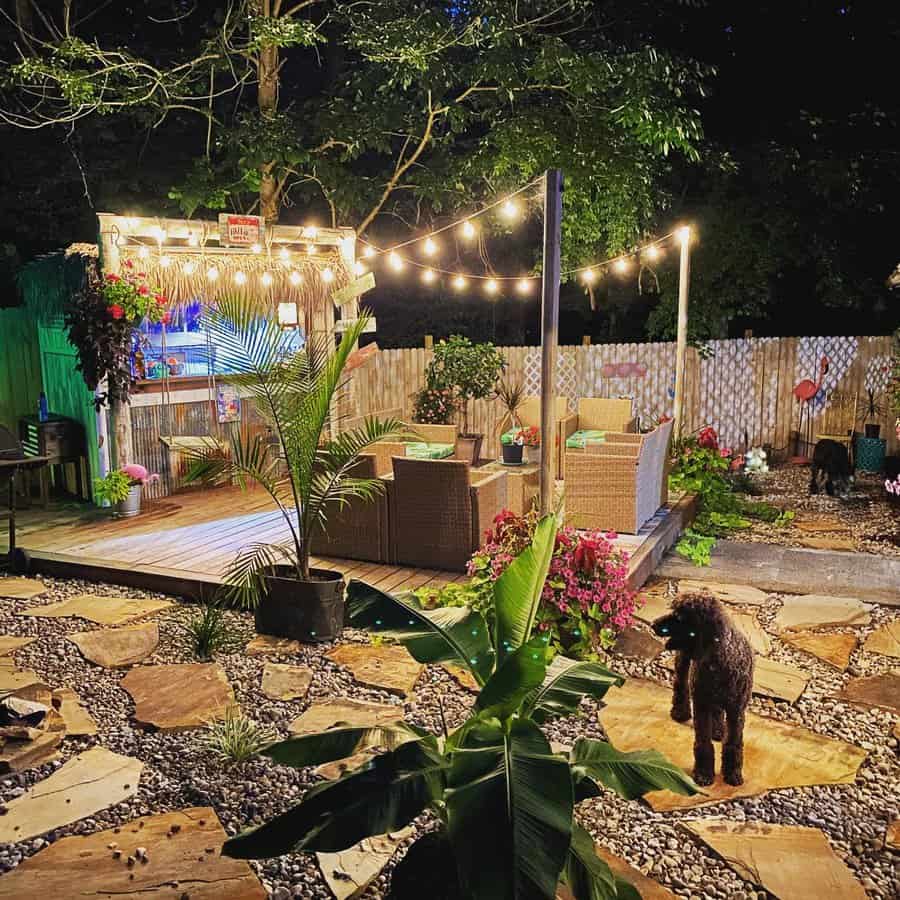 Backyard at night with string lights, patio furniture, plants, and a dog on stone path