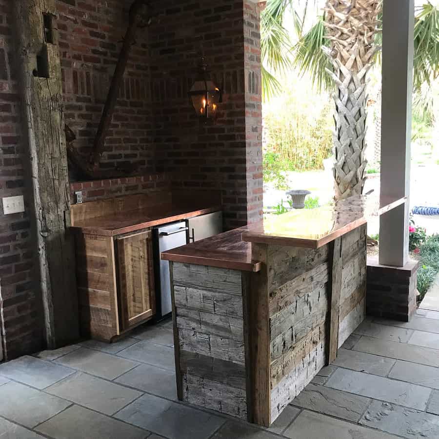 Outdoor rustic bar with wooden counter, brick walls, and a lantern hanging on the wall, palm tree in the background