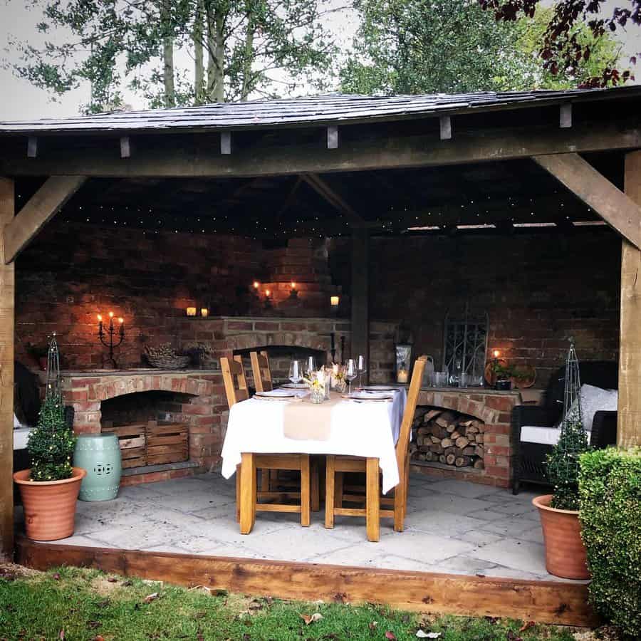 Cozy outdoor dining area with a wooden table, white tablecloth, candles, and potted plants under a rustic wooden gazebo