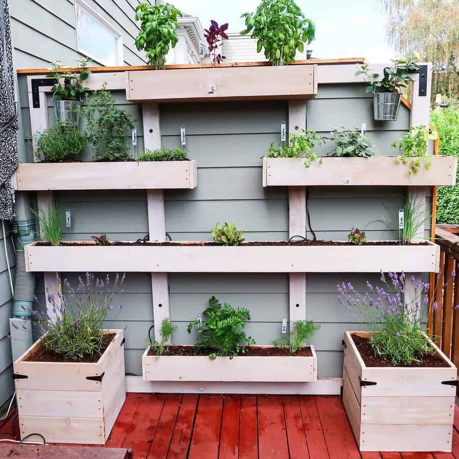 Vertical wooden pellet garden with multiple planters on a wall, featuring various herbs and plants, on a red deck