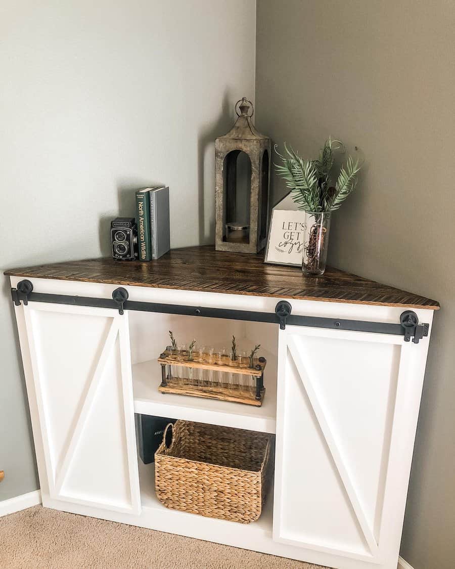 Rustic white corner cabinet with sliding barn doors and a dark wood top, styled with vintage decor, books, and greenery.