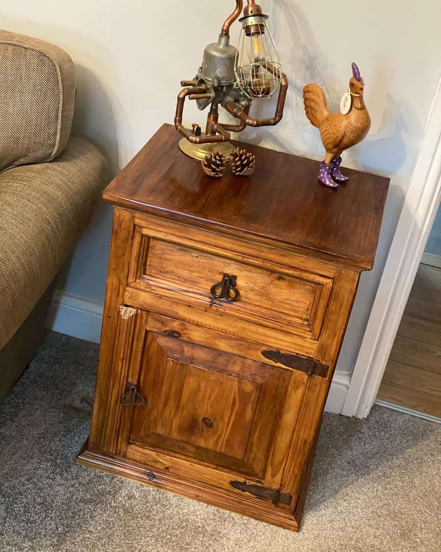 Rustic wooden nightstand with metal hardware, styled with a steampunk-inspired lamp and a decorative chicken figurine wearing boots.