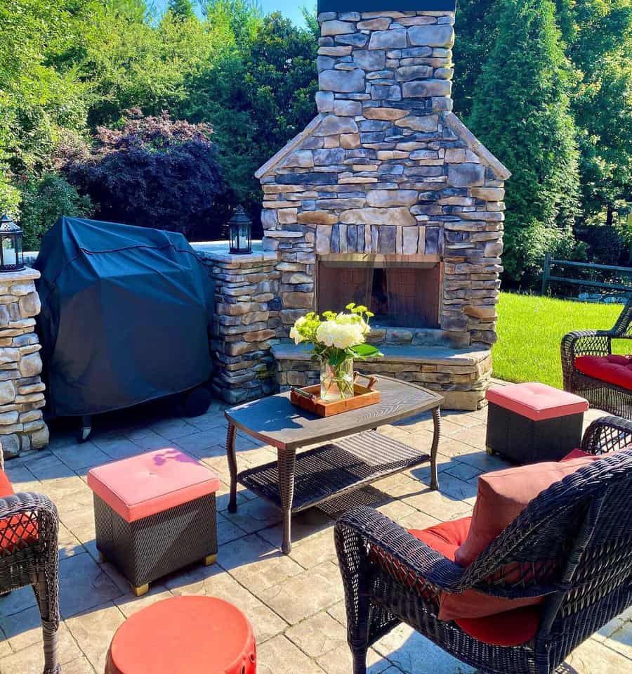 Outdoor patio with wicker furniture, red cushions, a stone fireplace, and a grill