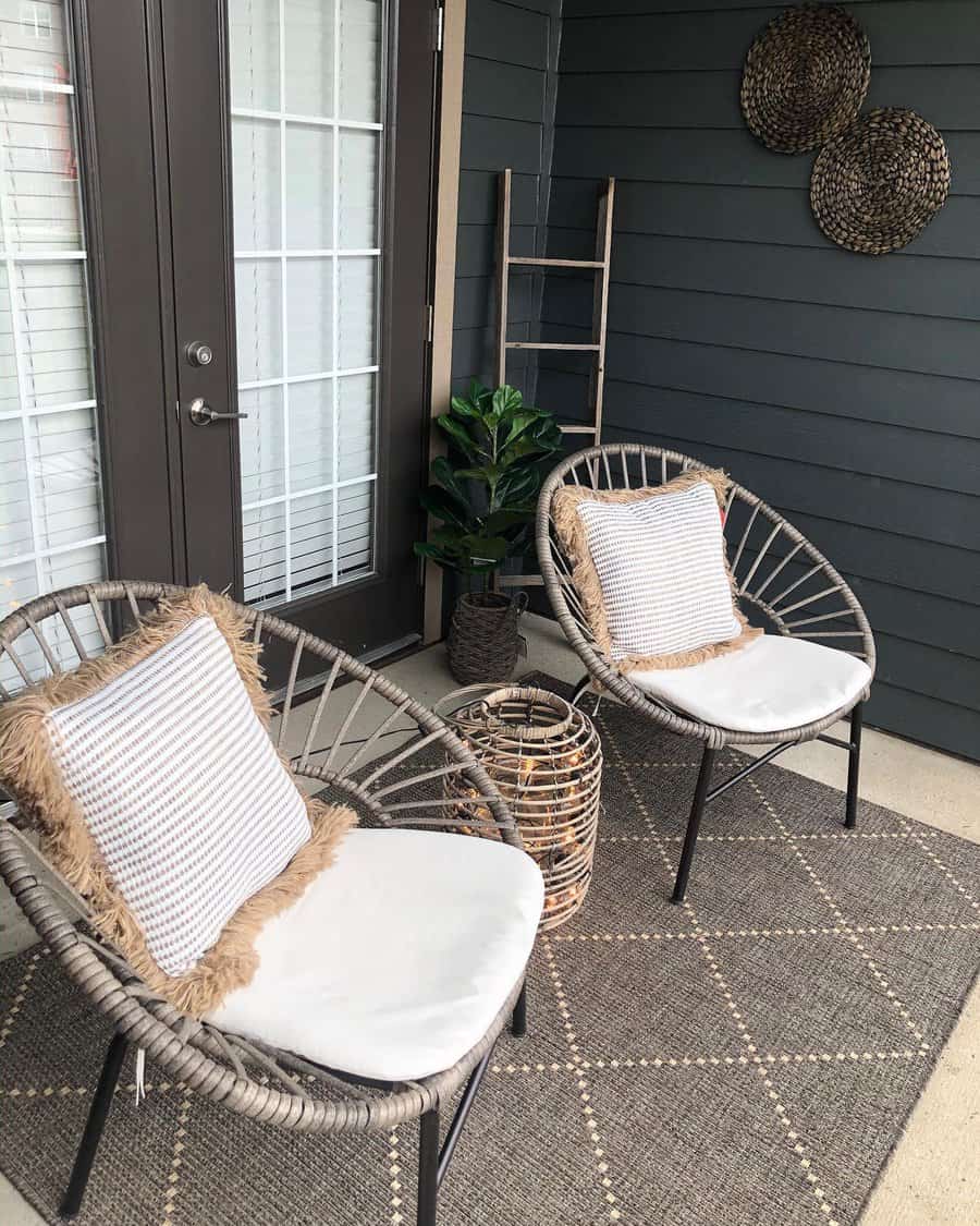 Cozy patio with two wicker chairs, white cushions, woven basket, small plant, and decorative wall hangings on dark paneled wall