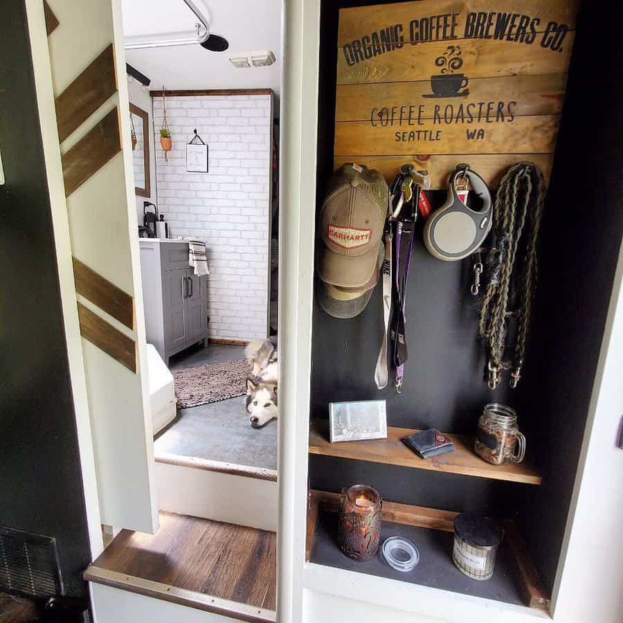 A rustic RV entryway with hooks for leashes and hats, wooden shelves with a photo and candles, creating a functional and cozy space. A dog rests in the background, adding to the homely feel.