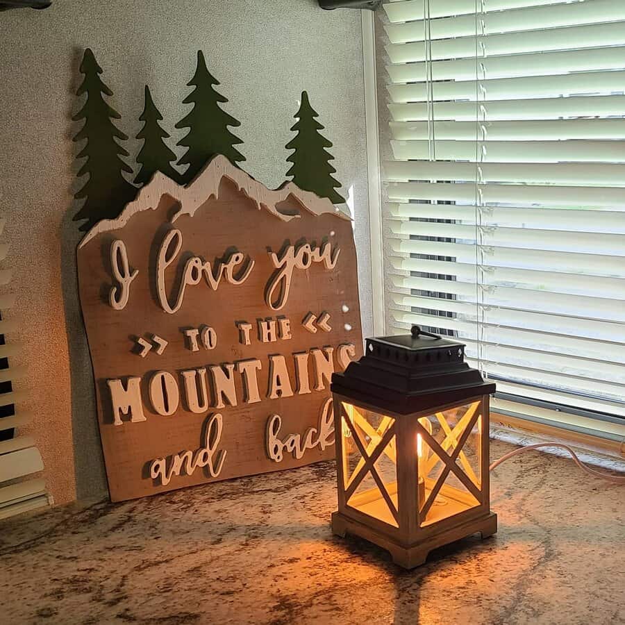 A charming RV corner with a rustic mountain-themed sign, a cozy lantern, and blinds, creating a warm and inviting atmosphere.