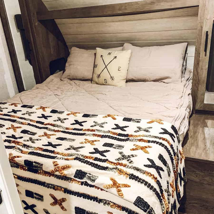 A cozy, rustic RV bedroom with neutral bedding, a decorative compass pillow, and a patterned throw blanket, creating a warm and inviting space.