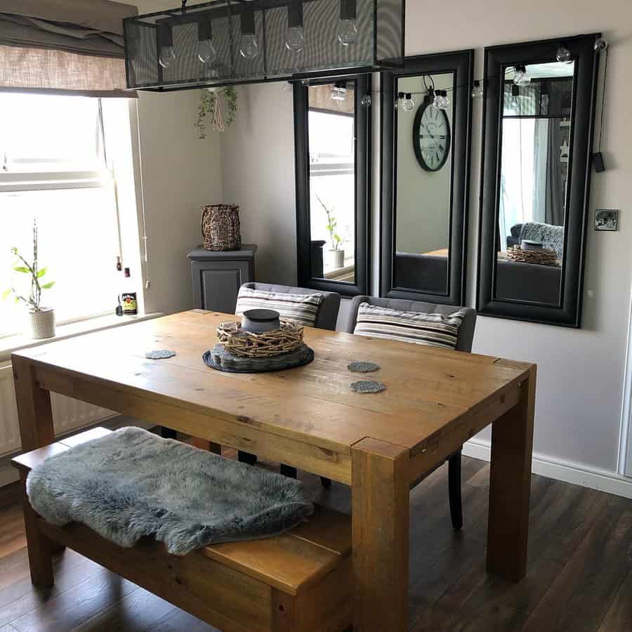 Dining room with a wooden table, bench, and chairs, featuring a modern chandelier, mirrors on the wall, and a large window on the left