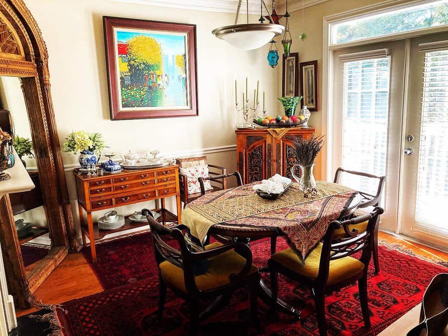 Eclectic dining room with colorful painting, patterned tablecloth, wooden furniture, rug, and glass doors; elegant and cozy atmosphere