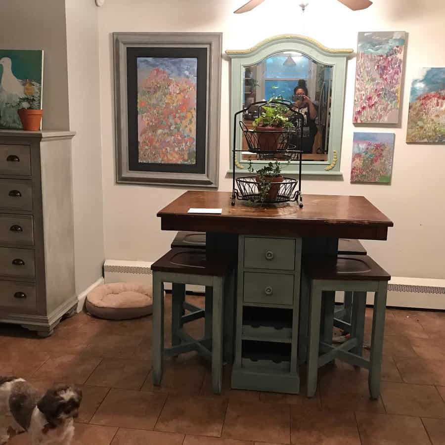 Rustic dining area with a wooden table, stools, and floral art on the walls