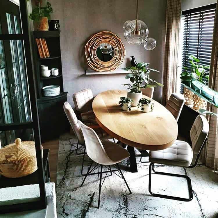 Rustic dining area with an oval wooden table, six chairs, plants, and decorative mirrors, lit by glass pendant lights