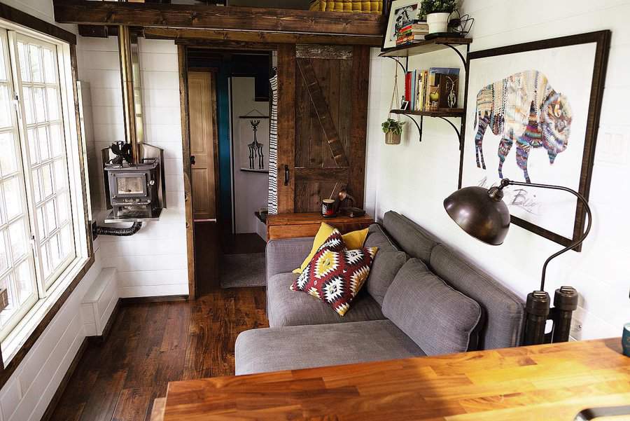 Rustic tiny living room with a gray sectional, wood-burning stove, barn door, warm wood tones, and tribal-patterned pillows for a cozy cabin feel