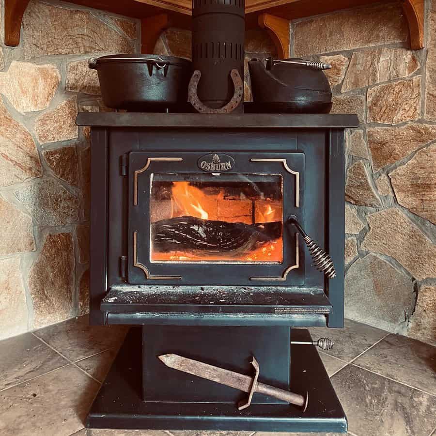 Rustic wood stove set against a stone hearth, adorned with cast iron cookware and a horseshoe for a warm, traditional cabin-style ambiance.