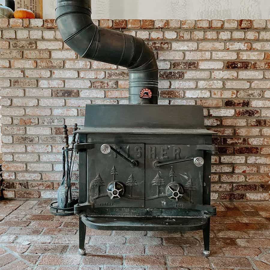 Vintage Fisher wood stove set against an exposed brick hearth, featuring rustic charm with intricate detailing and a curved chimney pipe.