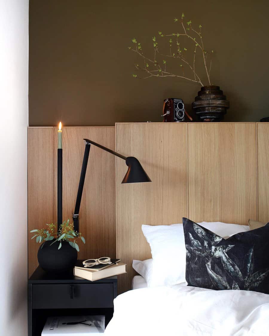 Scandinavian bedroom with wooden panel, green wall, and black nightstand featuring a tall candle, books, lamp, and black vase with greenery