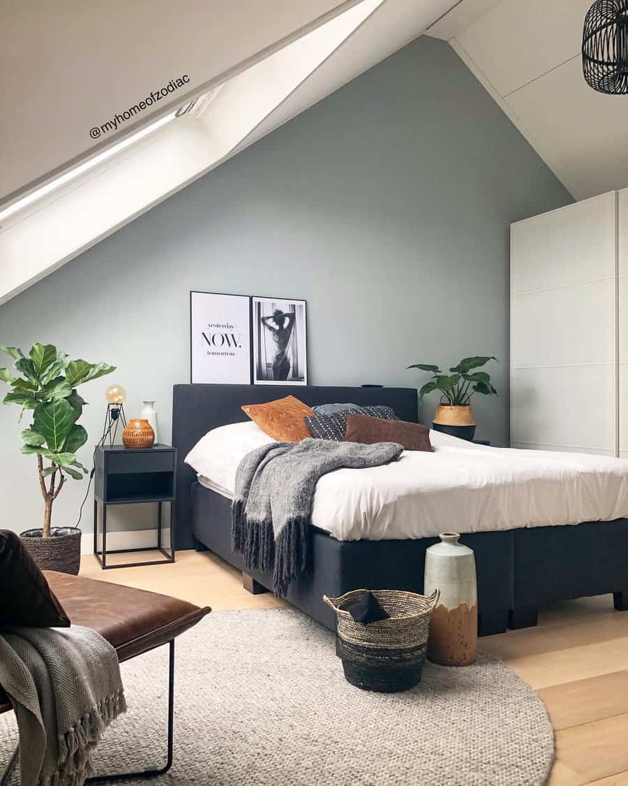 Scandinavian bedroom with a slanted ceiling, a bed with gray and brown accents, plants, and framed prints on a gray wall. Comfortable, modern decor.