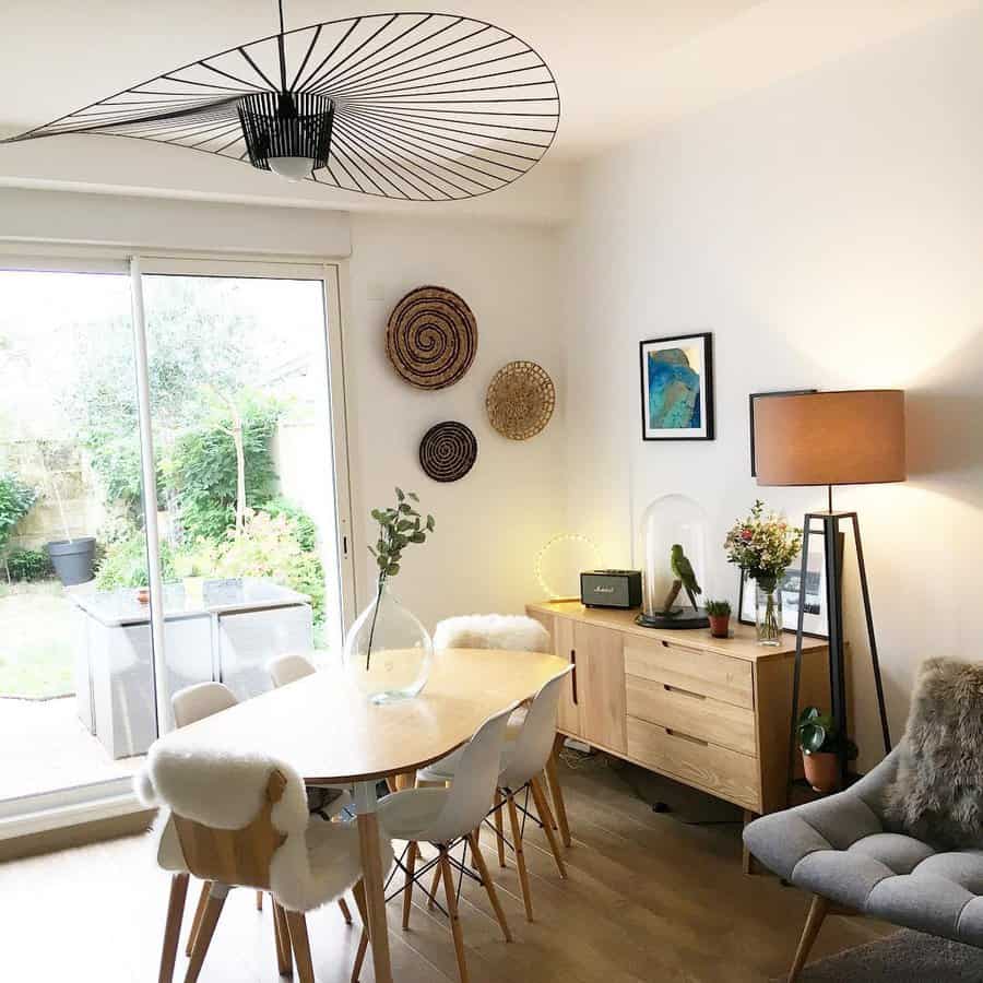 Modern dining room with a round table, white chairs, unique ceiling light, and wall decorations; glass doors open to a garden