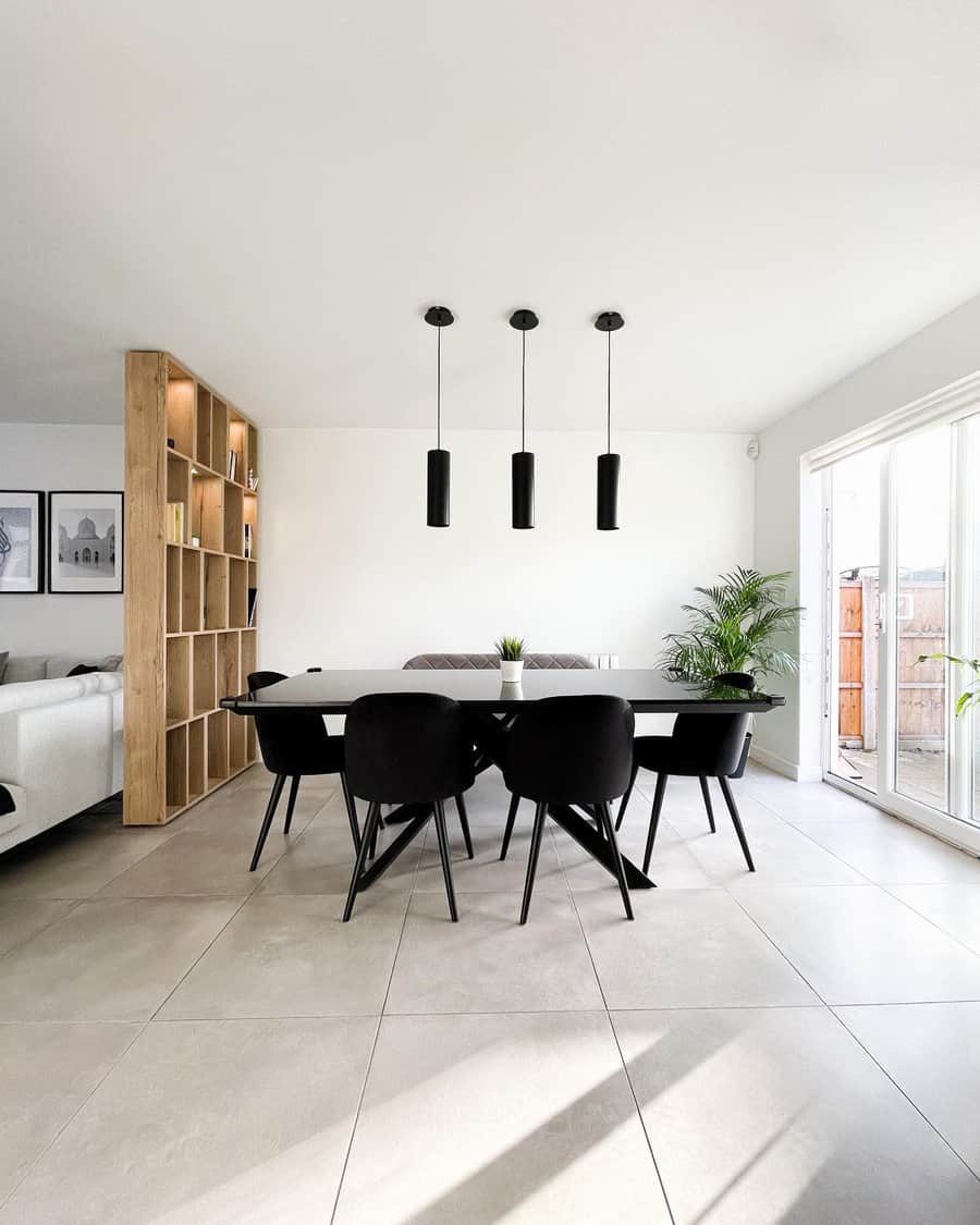 Modern dining room with a black table and six black chairs, pendant lights hang above, and a wooden shelf and plant are in the background