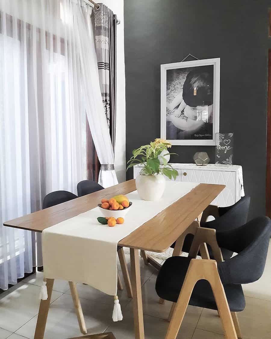 A modern dining room with a wooden table, black chairs, a plant centerpiece, and a bowl of fruit, complemented by large photo and decor on the wall