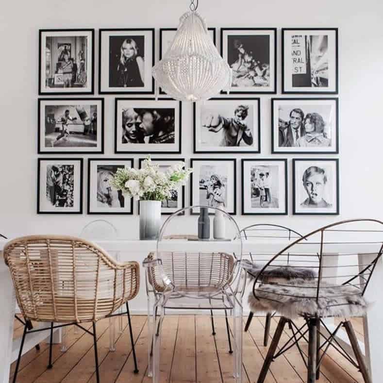 Eclectic dining area with a white table, diverse chairs, and a wall of black-and-white photos, with a chandelier hanging above