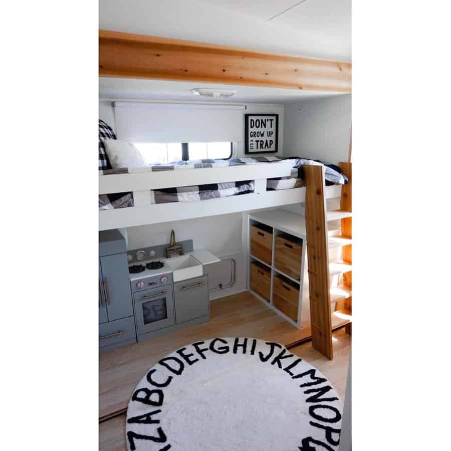 A Scandinavian-style RV bedroom with a loft bed, a playful alphabet rug, a small kitchen area, and organized storage, creating a cozy and functional living space.