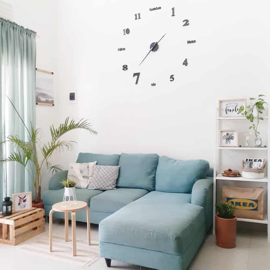 Minimalist Scandinavian living room with a soft blue sectional, large wall clock, greenery, and light wood accents for a fresh and airy feel