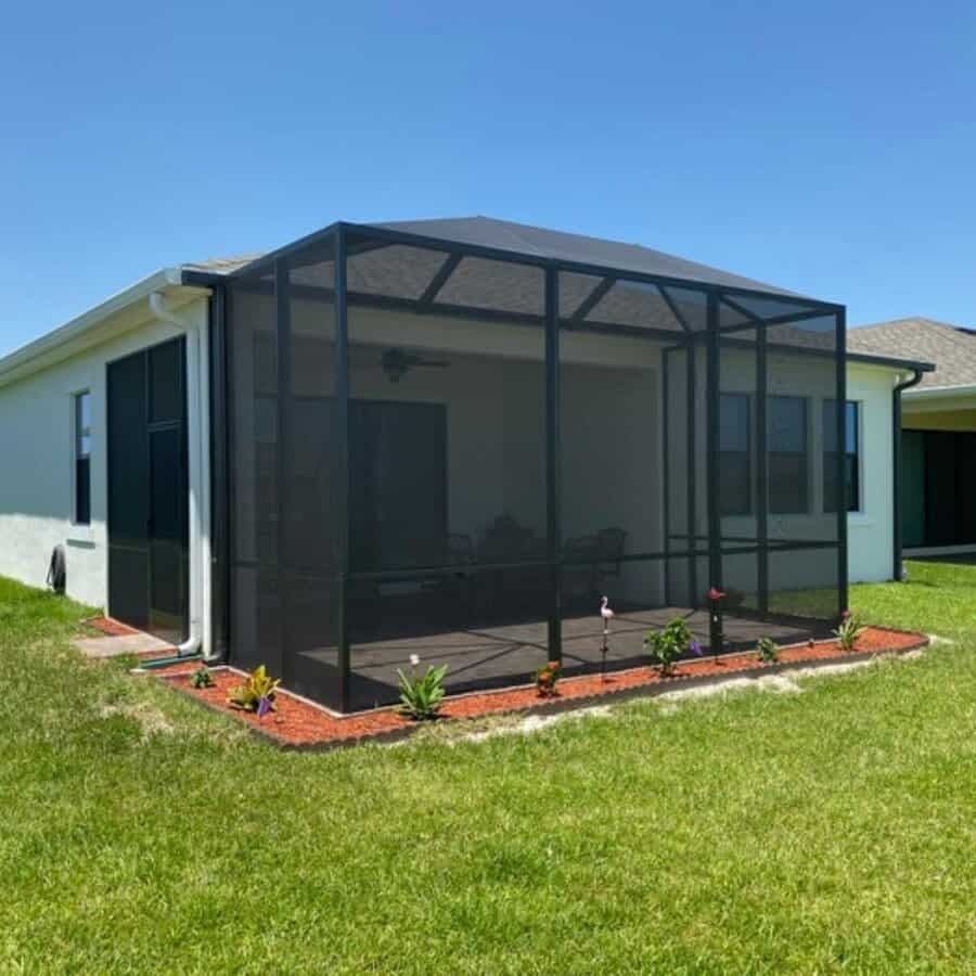 A house with a screened-in patio featuring a small garden with plants, under a clear blue sky