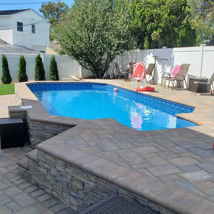 Semi-in-ground pool with elegant stone edging, a paved patio, and cozy seating, creating a stylish and inviting backyard retreat