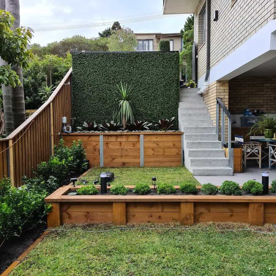 Modern backyard with wooden planters, green hedge, and concrete stairs leading to a house