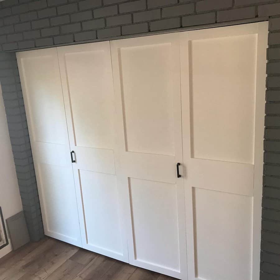 White sliding closet doors with black handles, set against a gray brick wall