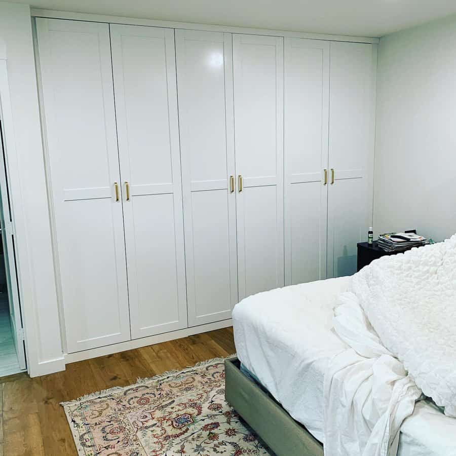 White built-in wardrobes in a bedroom with a bed and patterned rug on a wooden floor