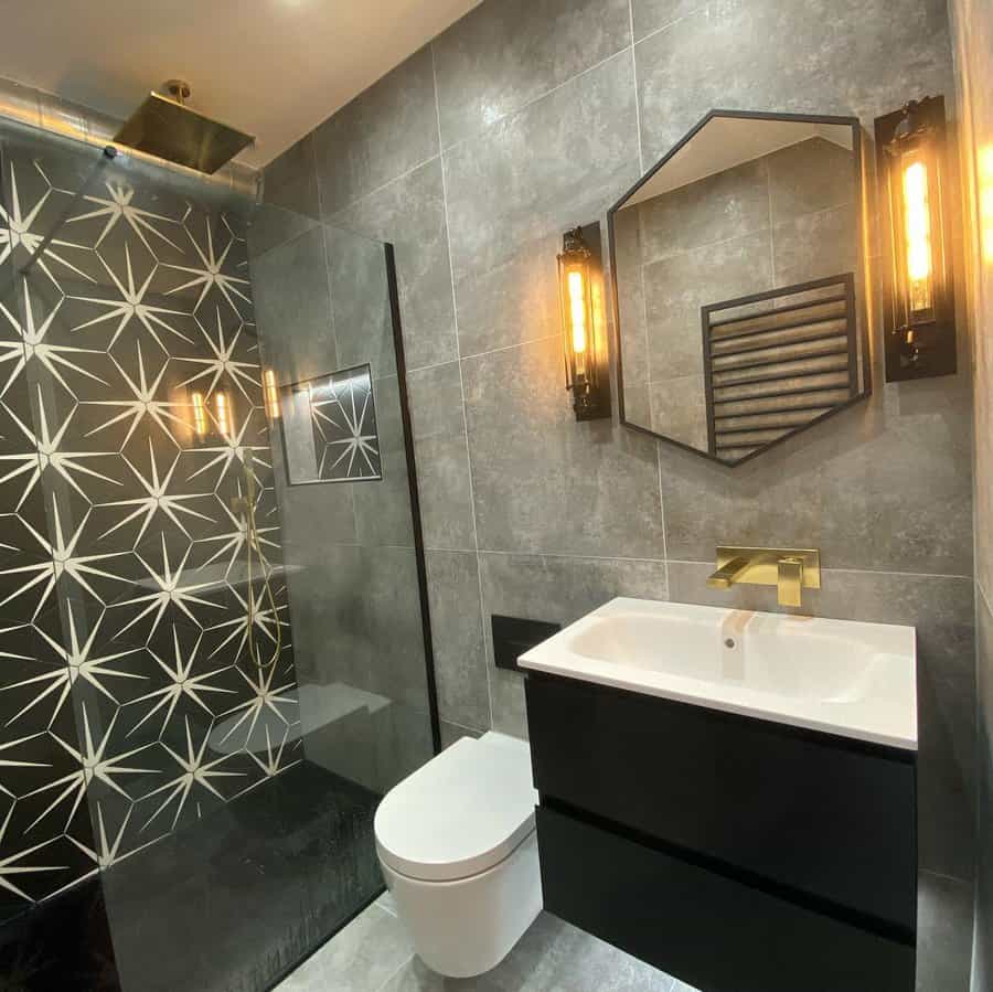 Modern bathroom featuring a geometric shower wall, an octagonal mirror, wall lights, gold fixtures, and a black and white sink and toilet setup