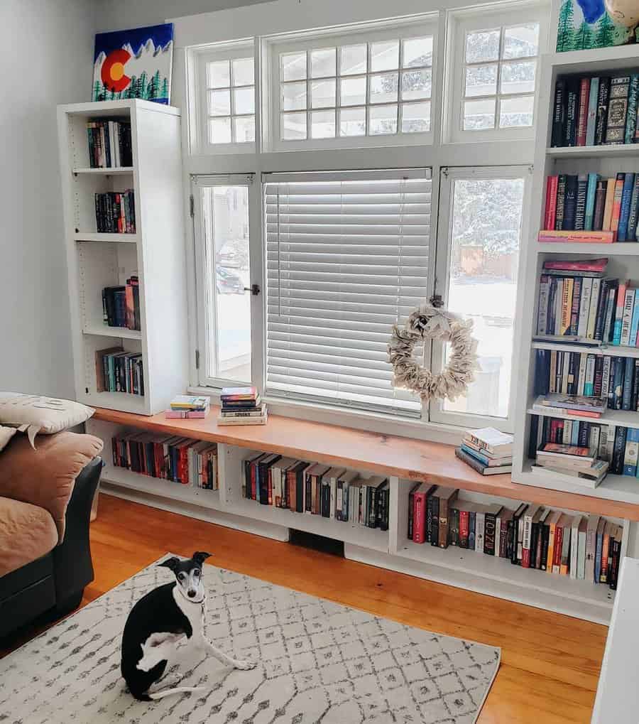 Cozy reading nook with built-in bookshelves and a wooden bench under large windows, featuring a relaxed dog on a patterned rug.