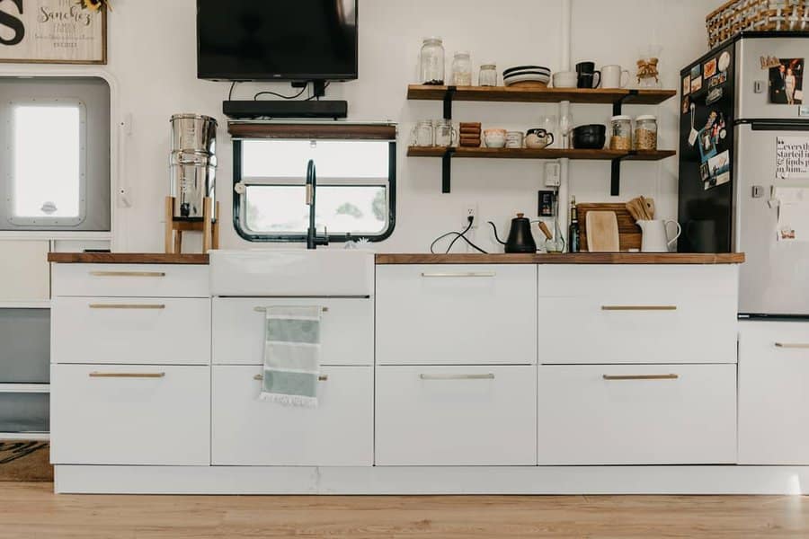 Minimalist RV kitchen with white cabinetry, open wood shelves, a farmhouse sink, and a neatly organized space for stylish functionality.