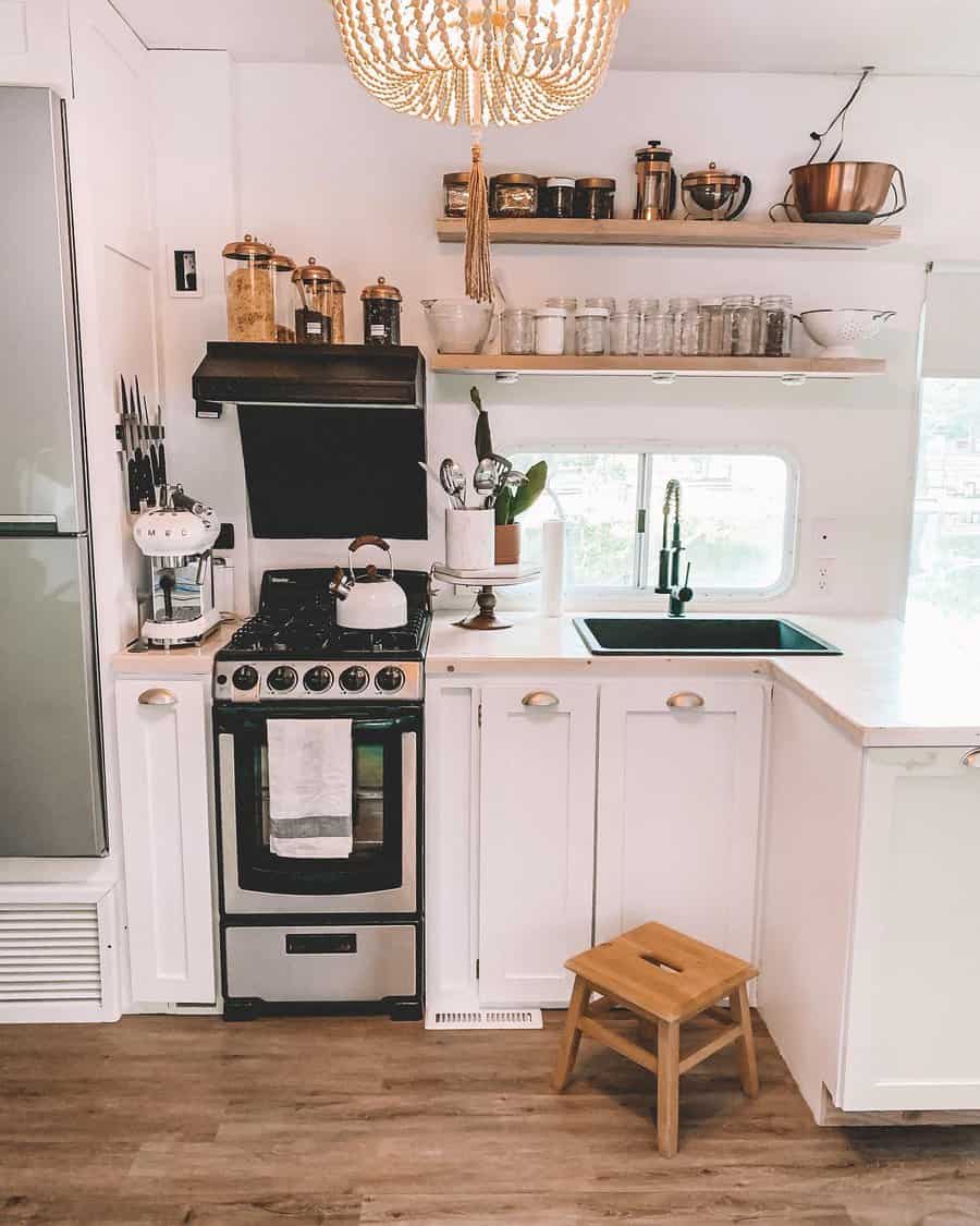 Chic RV kitchen with white cabinetry, open wood shelves, glass storage jars, and a black farmhouse sink, blending function with style.