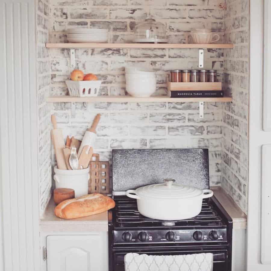 Rustic RV kitchen with open wood shelves, a brick backsplash, and neatly arranged cookware, creating a cozy farmhouse-inspired space.