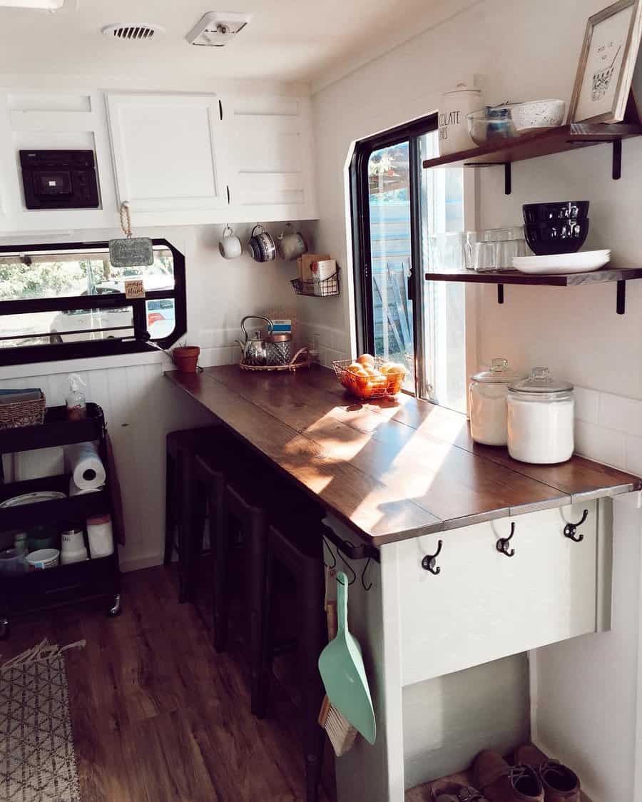 Cozy RV kitchen with open shelves, a wooden countertop with tucked-in stools, hanging storage, and a rolling cart for extra organization.